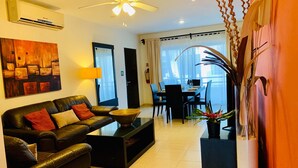 A modern living room with a leather sofa, a coffee table, and a dining area with a table and chairs. - Condo Pacifico by Playa Paradise (Playa del Carmen)