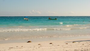 A beach with clear turquoise water, a sandy shore, and a few boats. - Condo Pacifico by Playa Paradise (Playa del Carmen)