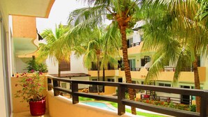 A balcony with a view of a pool, palm trees, and a building with balconies. - Condo Pacifico by Playa Paradise (Playa del Carmen)