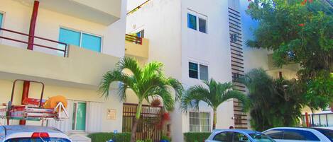 Un edificio residencial de varios pisos con balcones, una moto estacionada y un automóvil.