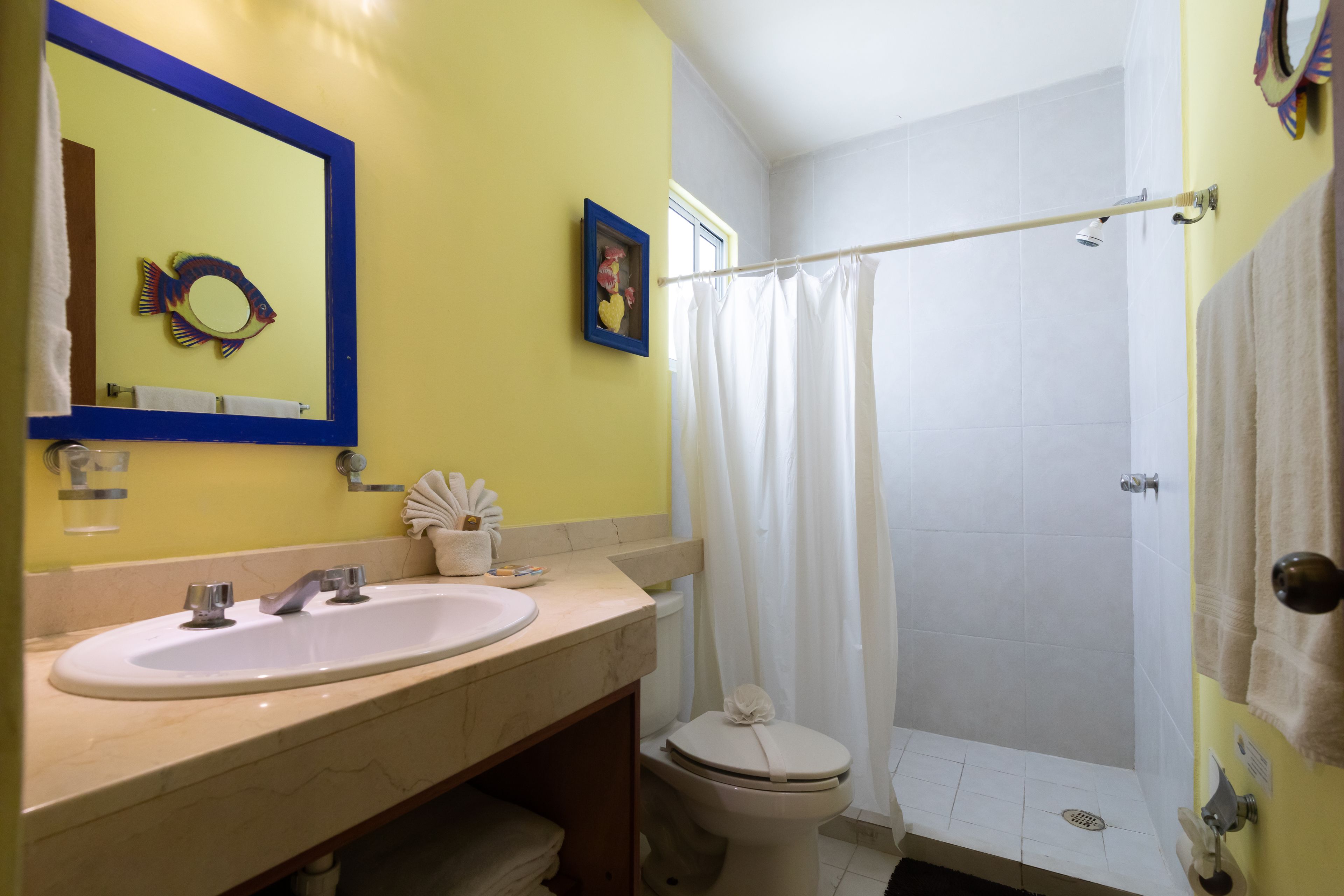 A bathroom with a yellow wall, a white sink, a mirror, a toilet, and a shower curtain.