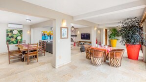 A spacious living area with a dining table, chairs, a sofa, and a TV. There are potted plants and artwork on the walls. - Casa Bahia Linda by Kivoya (Puerto Vallarta)