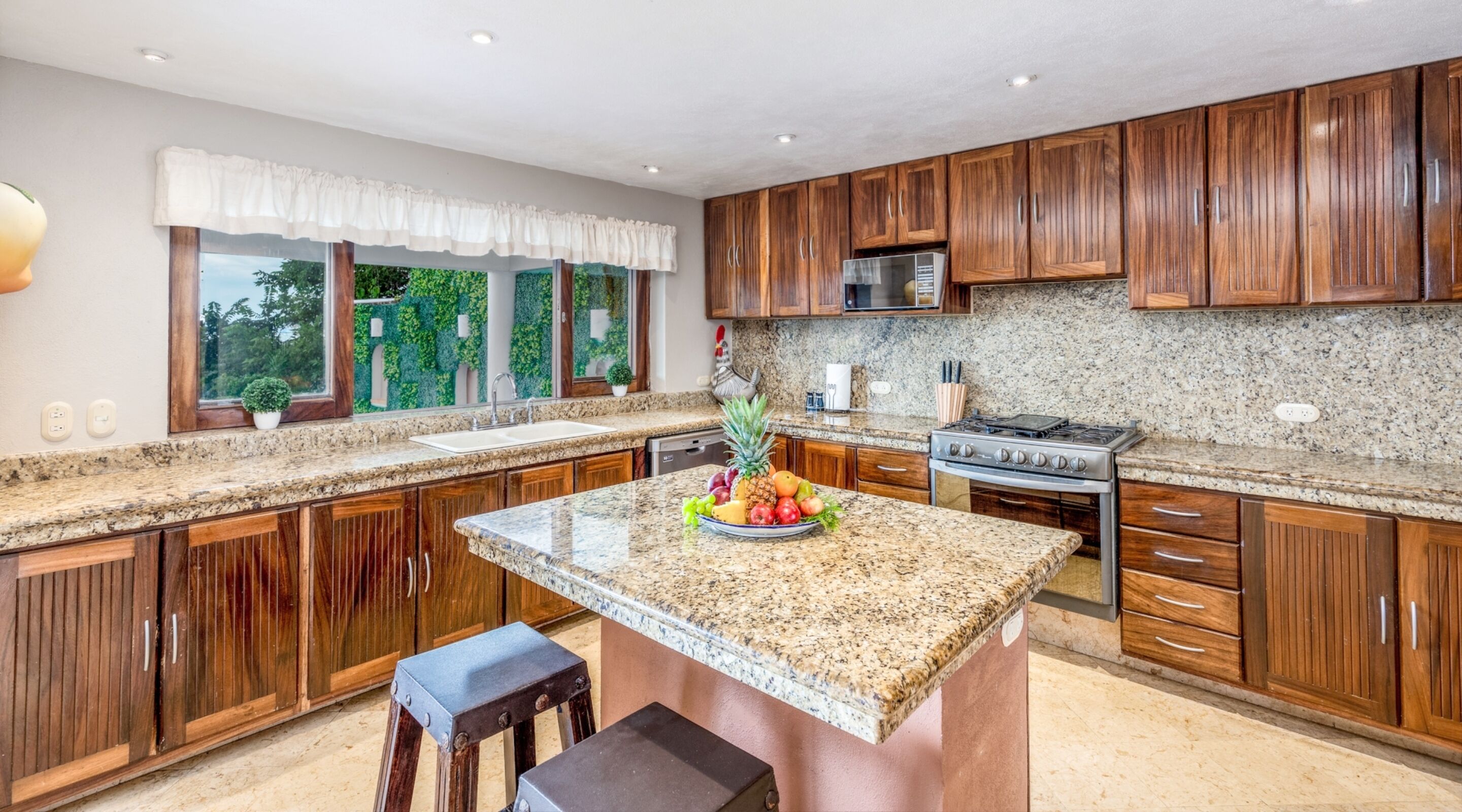 A kitchen with wooden cabinets, granite countertops, a central island with fruit, and a built-in stove.