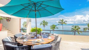 A dining area with a table set for two, overlooking a scenic ocean view with palm trees. - Casa Bahia Linda by Kivoya (Puerto Vallarta)