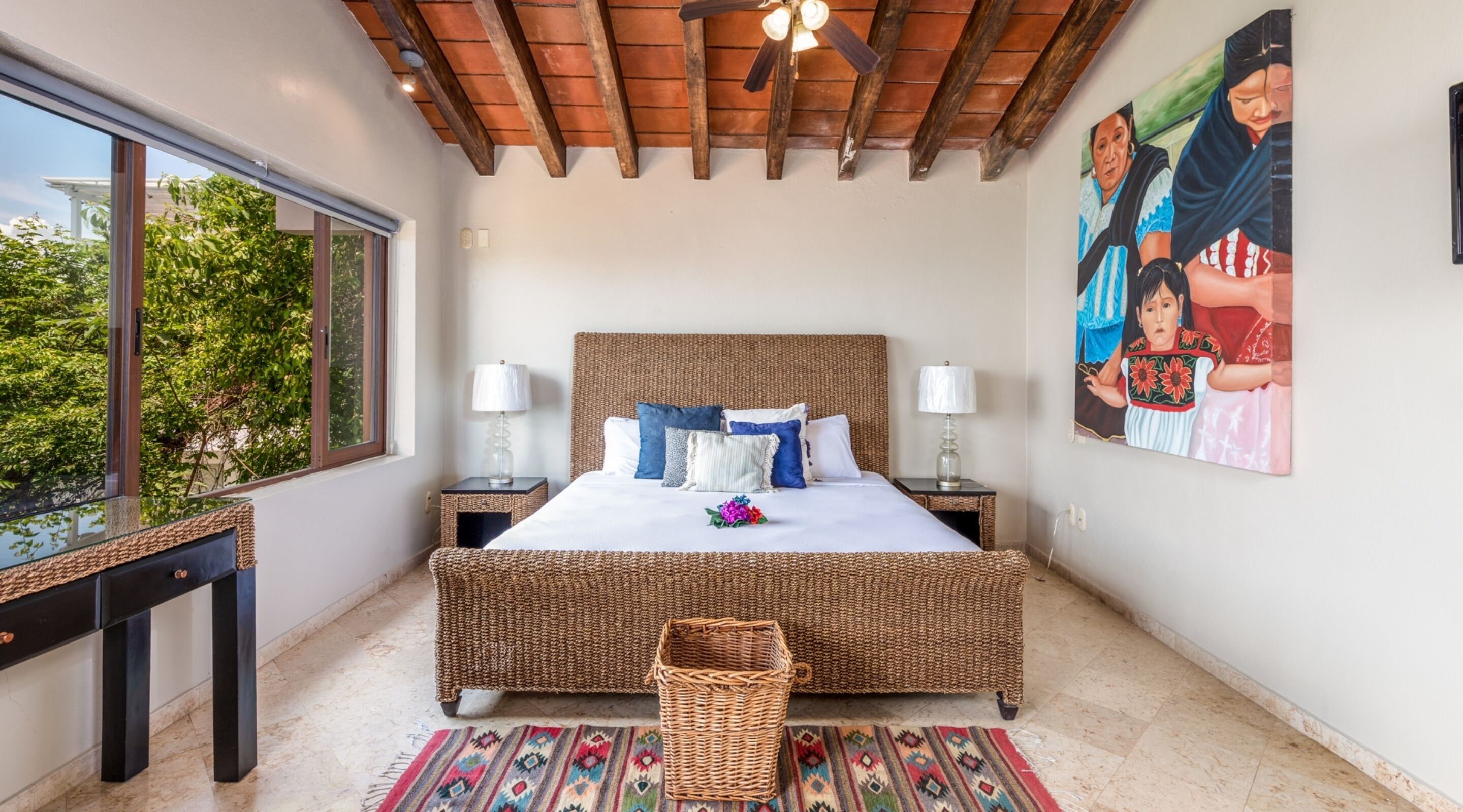 A spacious bedroom with a large bed, two bedside tables, a ceiling fan, and a window with a view of greenery.