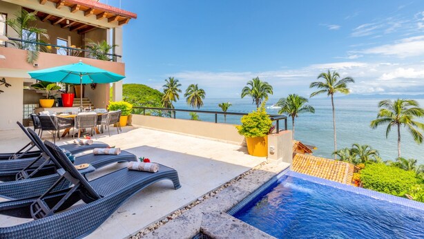 A poolside area with lounge chairs, a table, and a view of the ocean. - Casa Bahia Linda by Kivoya (Puerto Vallarta)