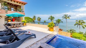 A poolside area with lounge chairs, a table, and a view of the ocean.