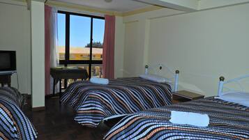 A hotel room with three beds, a television, and a window with a view of buildings outside.