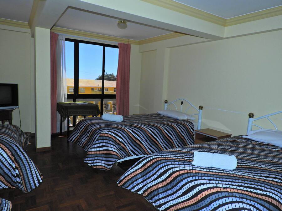 A hotel room with three beds, a television, and a window with a view of buildings outside.