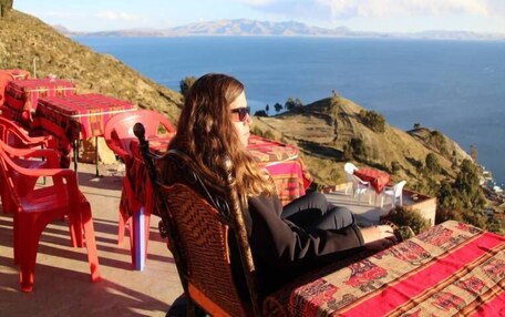 A person seated on a chair with a view of a body of water and hills in the background.