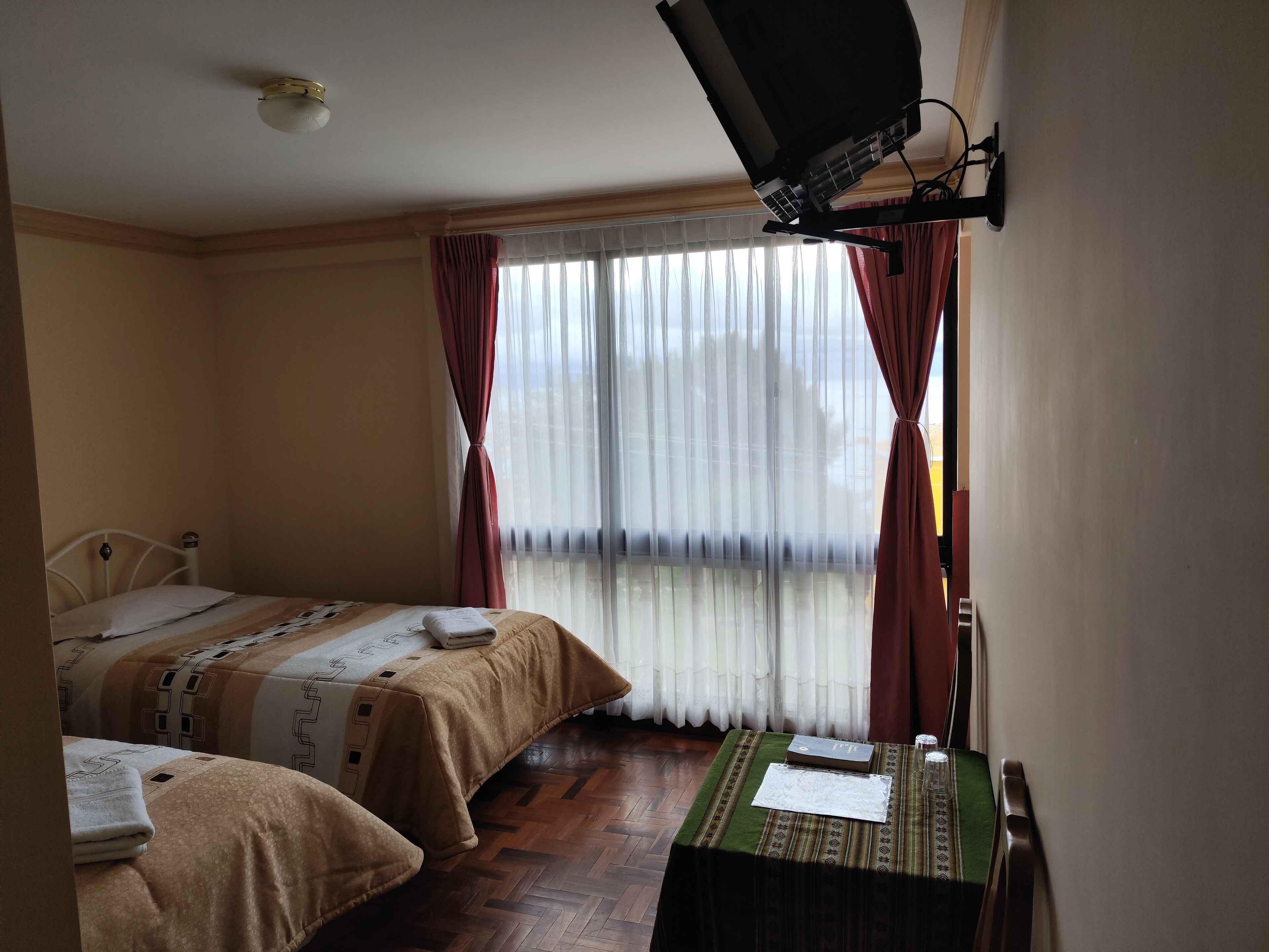 Une chambre d’hôtel avec deux lits, un bureau avec un ordinateur, un téléviseur fixé au mur et une fenêtre avec des rideaux légers.