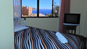 A room with a bed, a television, and a window with a view of the sea and buildings. - Hotel Wendy Mar (Copacabana)