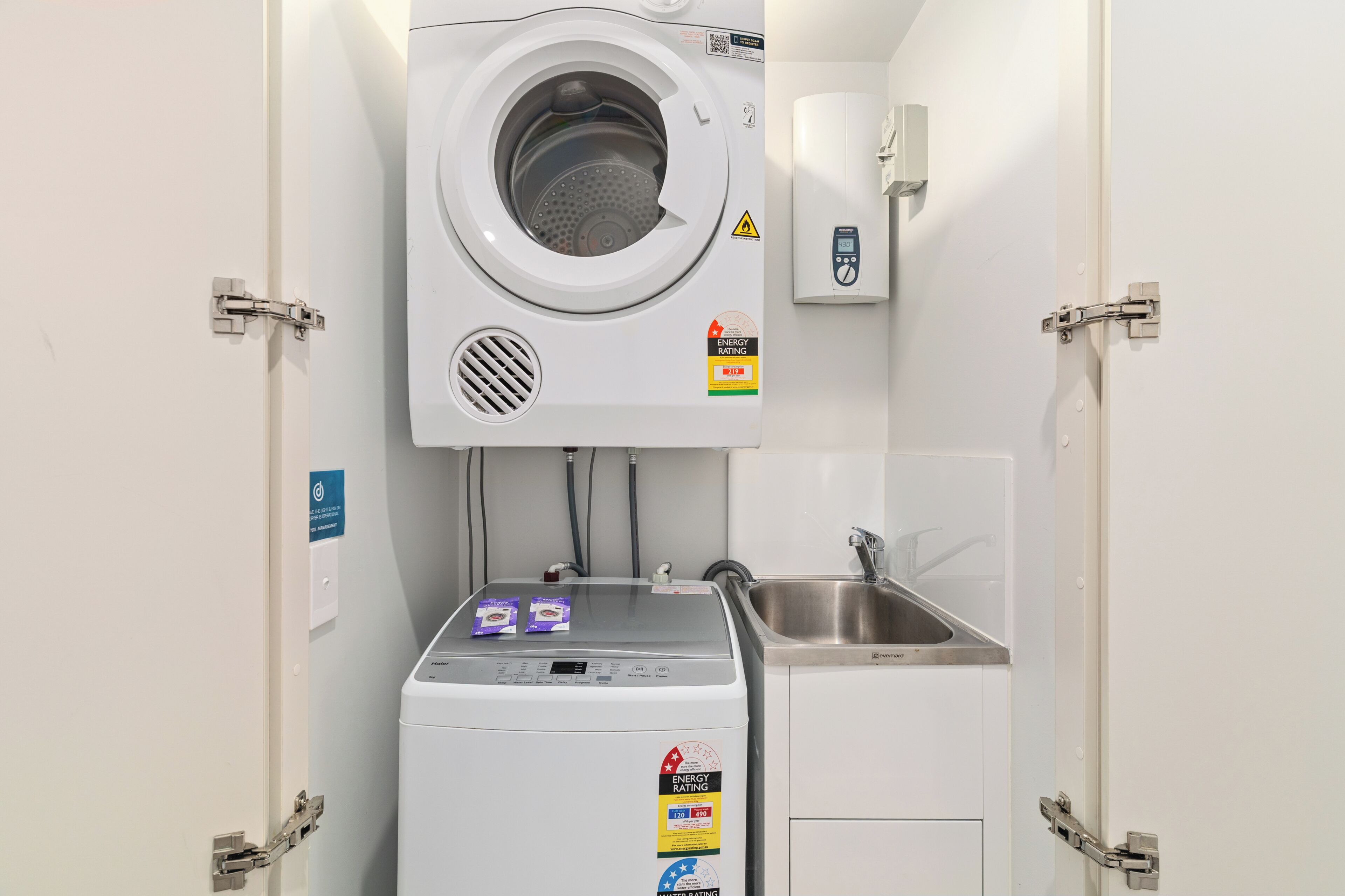 Uma lavanderia compacta com máquina de lavar e secadora frontais, um aquecedor fixado na parede e uma pia.