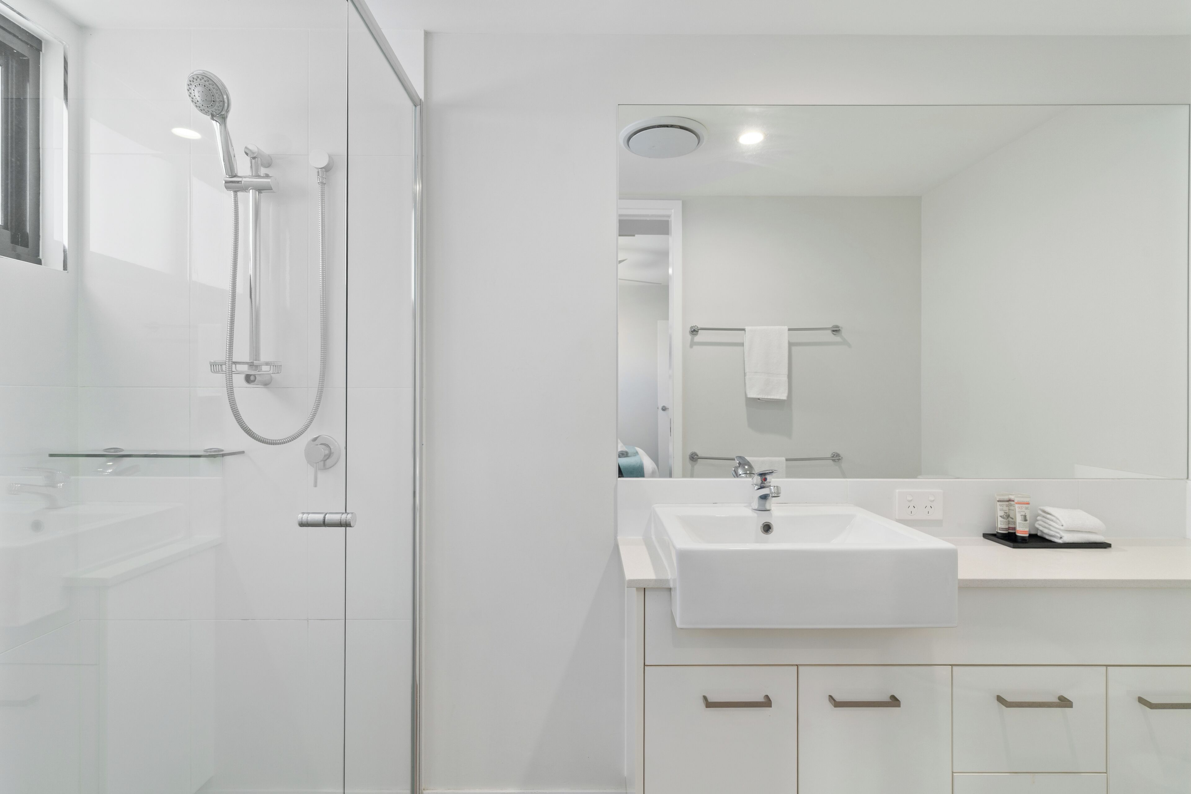 A modern bathroom with a glass shower enclosure, a white sink, and a large mirror.