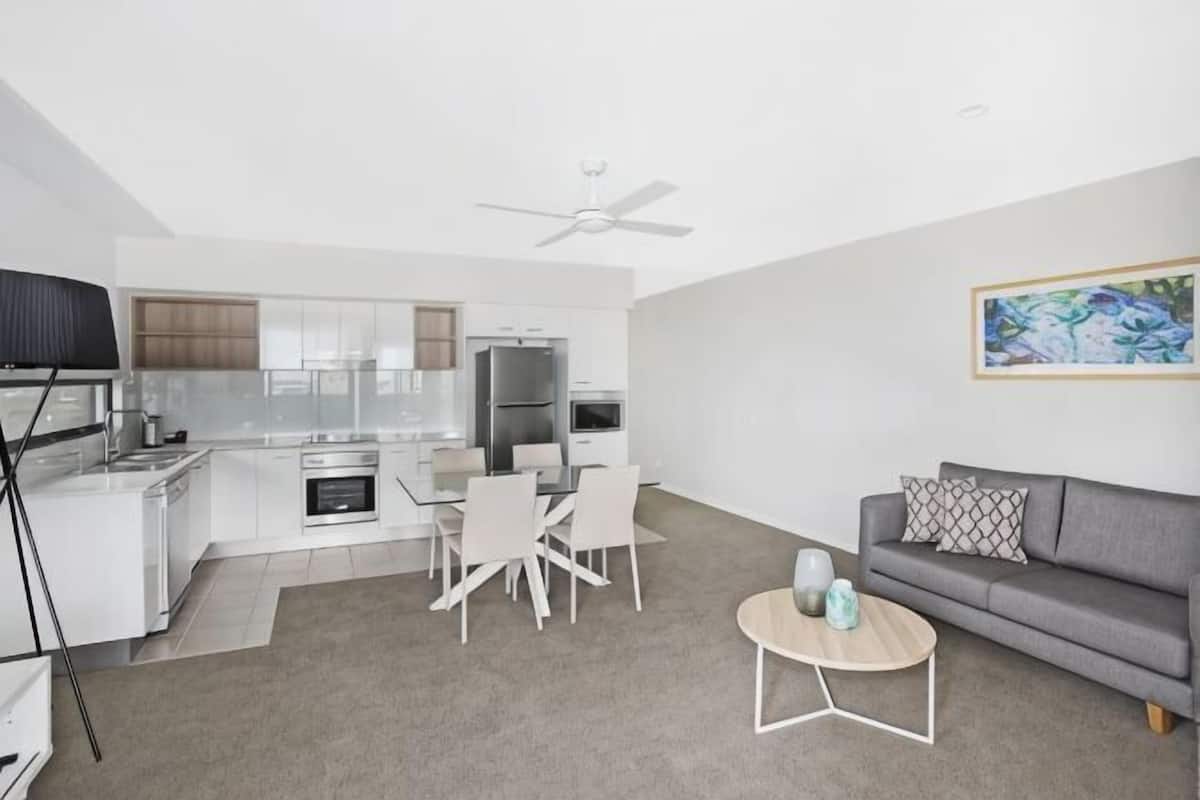 A modern living room with a grey sofa, a coffee table, and a dining area with chairs and a table.