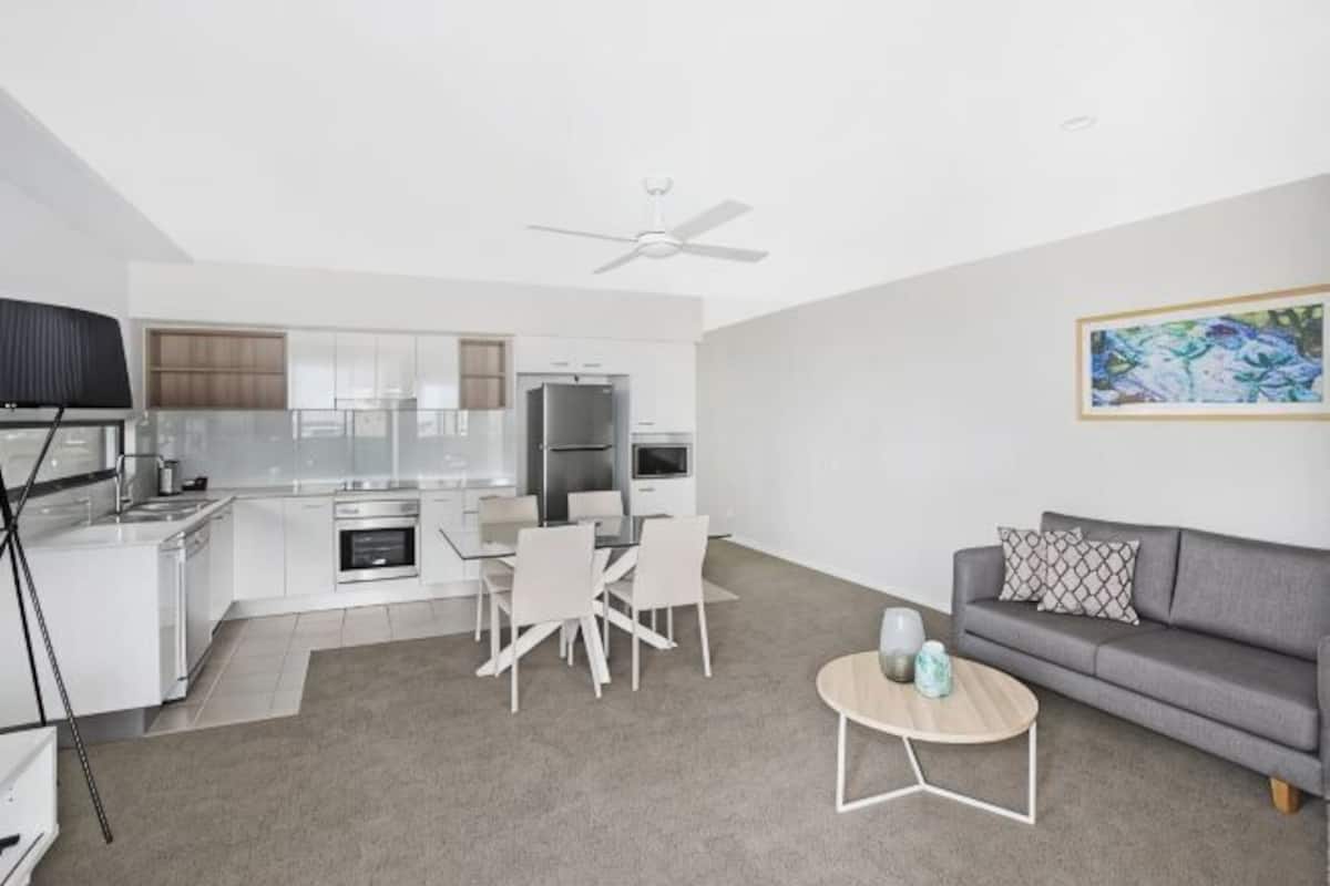 A modern living room with a grey sofa, a coffee table, and a dining area with chairs and a table.