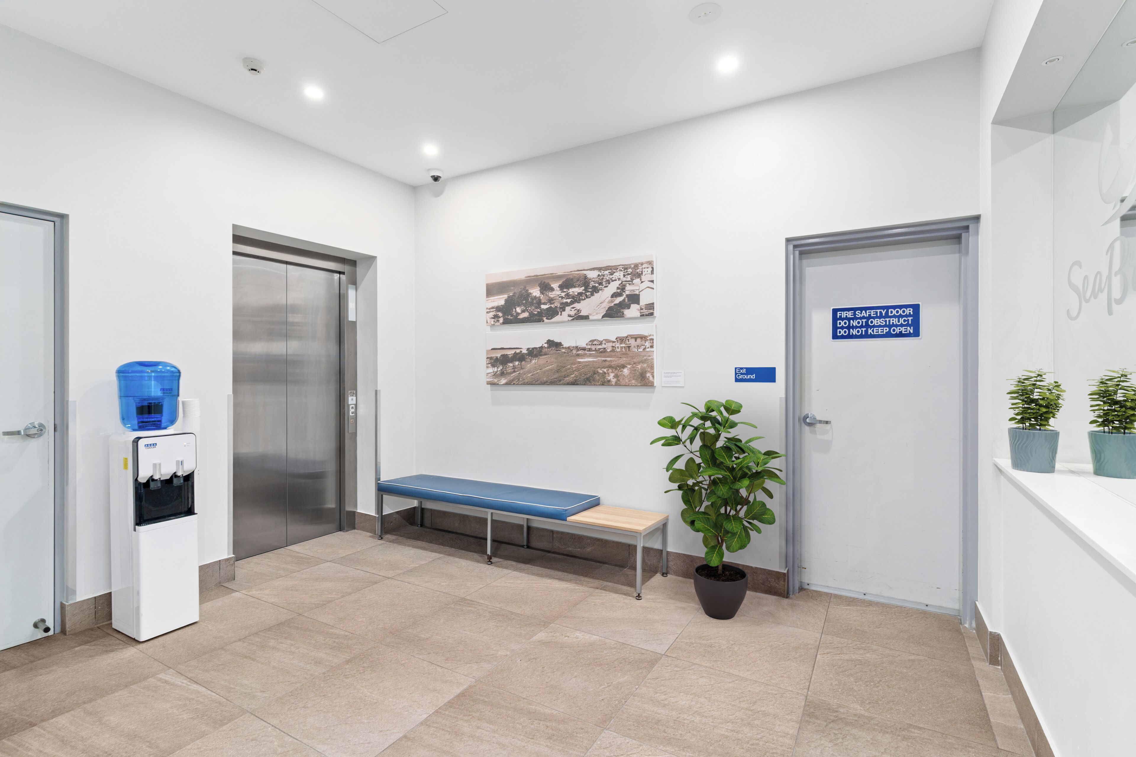 A reception area with a water dispenser, a bench, a potted plant, and a fire safety sign.