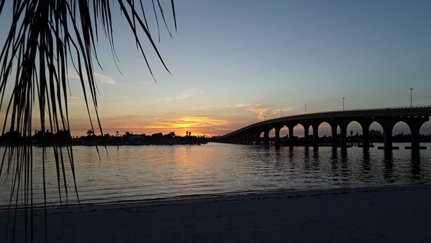 Un atardecer sobre un puente, con agua al frente.