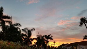 Un coucher de soleil avec des palmiers et un bâtiment au premier plan.