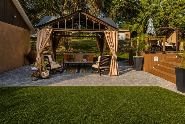 A covered outdoor seating area with a pergola, cushioned seating, and a patterned rug.
