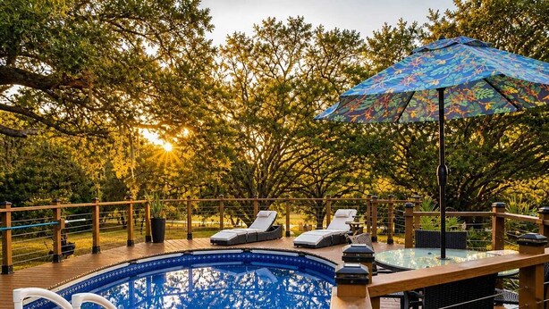Ein Poolbereich mit Holzterrasse, Liegestühlen, einem Glastisch und einem Zier-Sonnenschirm.