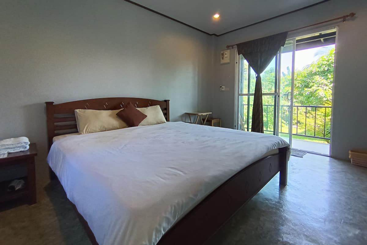 Une chambre à coucher avec un grand lit, une table de chevet, une petite table et une fenêtre donnant sur un paysage verdoyant.