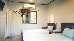 A bedroom with two beds, a window with curtains, a wall-mounted air conditioner, and a small bedside table with a lamp.