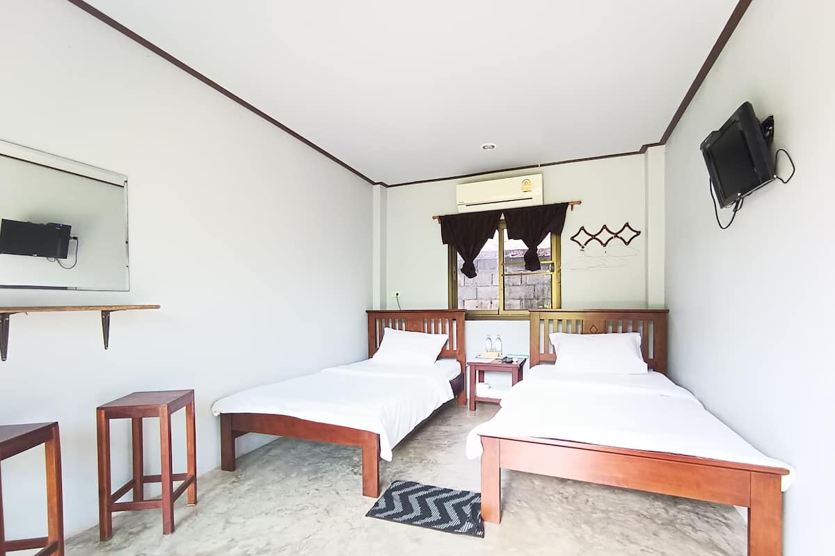 Une chambre d’hôtel avec deux lits simples, une petite table, un téléviseur fixé au mur et une fenêtre avec des rideaux.