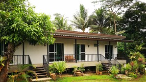 A house with a porch, steps leading to a door, and a small garden area with potted plants and a tree.