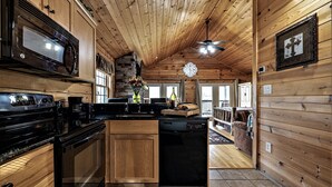 A wooden cabin interior with a kitchen featuring a stove, microwave, and dishwasher.