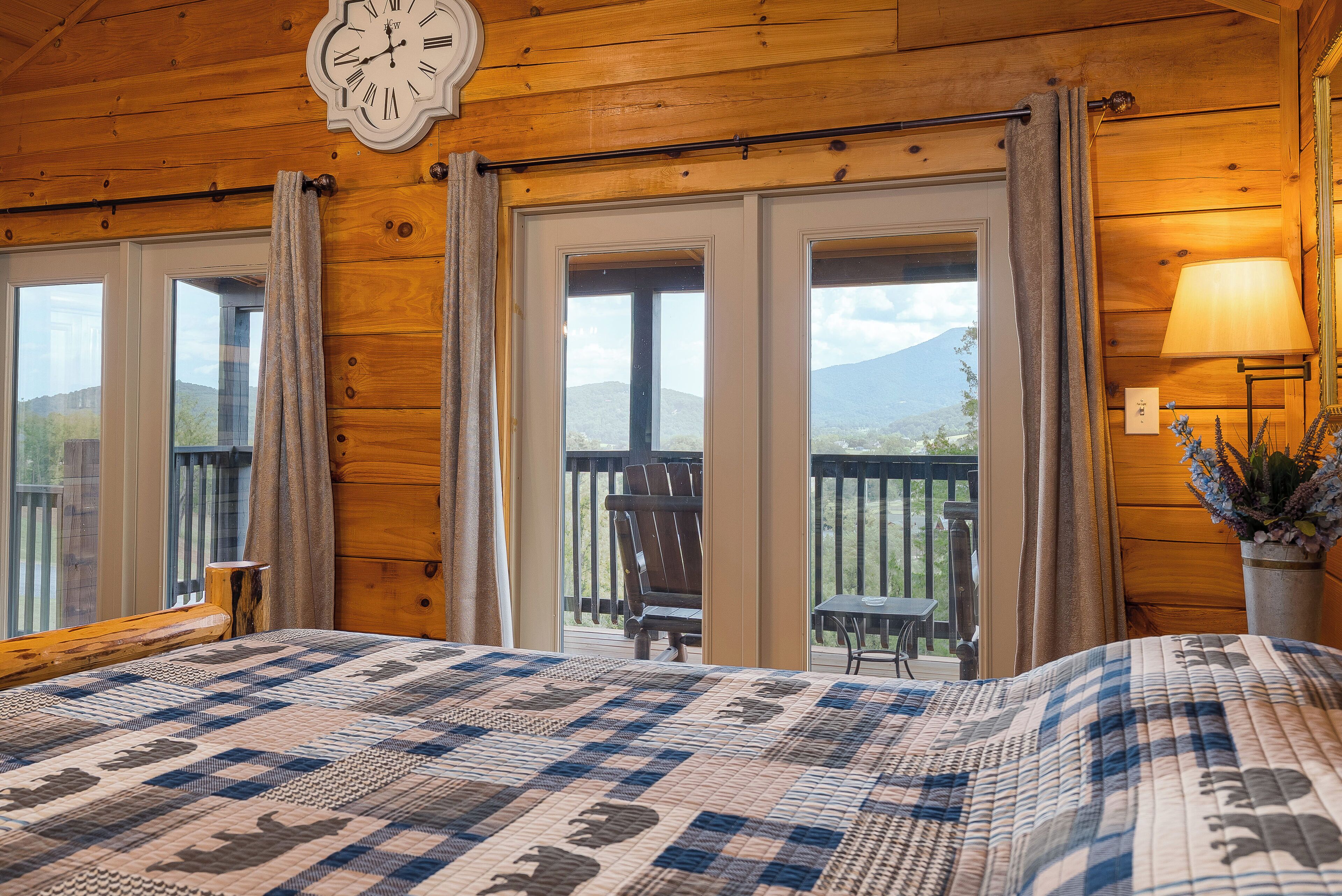 Une chambre dans un chalet en bois, avec un lit, une horloge et un balcon équipé d’une chaise.
