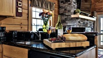 Une cuisine avec des meubles de rangement en bois, un mur en pierre, un plan de travail en bois, un lave-vaisselle et une planche à découper avec des fruits et une bouteille.
