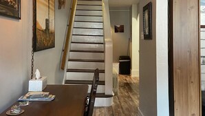 A wooden dining table with a tissue box and magazines, a staircase with a wooden railing, and a hanging light fixture. - Spacious 3 Bedroom, 2 Bath Apartment-historic Jim Thorpe, large patio & balcony (Jim Thorpe)