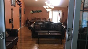A spacious living room with a black leather sofa, a dining area with wooden chairs, and a chandelier. - 6 BDRM BEAUTIFUL HOME ON ONE FLOOR "LIONS DEN" -Big Boulder,Camelback,Jack Frost (Lake Harmony)