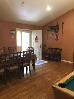 Un coin repas avec une table et des chaises en bois, un billard et une porte décorée d’un nœud rouge.