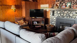 Ein gemütliches Wohnzimmer mit Kamin aus Stein, Holzwänden und einem großen grauen Ecksofa.
