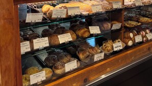 Eine Backvitrine mit verschiedenen Backwaren wie Muffins, Croissants und Brötchen, jedes mit Preisen beschriftet.