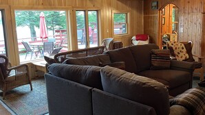 Ein gemütliches Blockhaus-Interieur mit einem großen grauen Sofa, Korbstühlen und einem Essbereich mit einem roten Sonnenschirm.