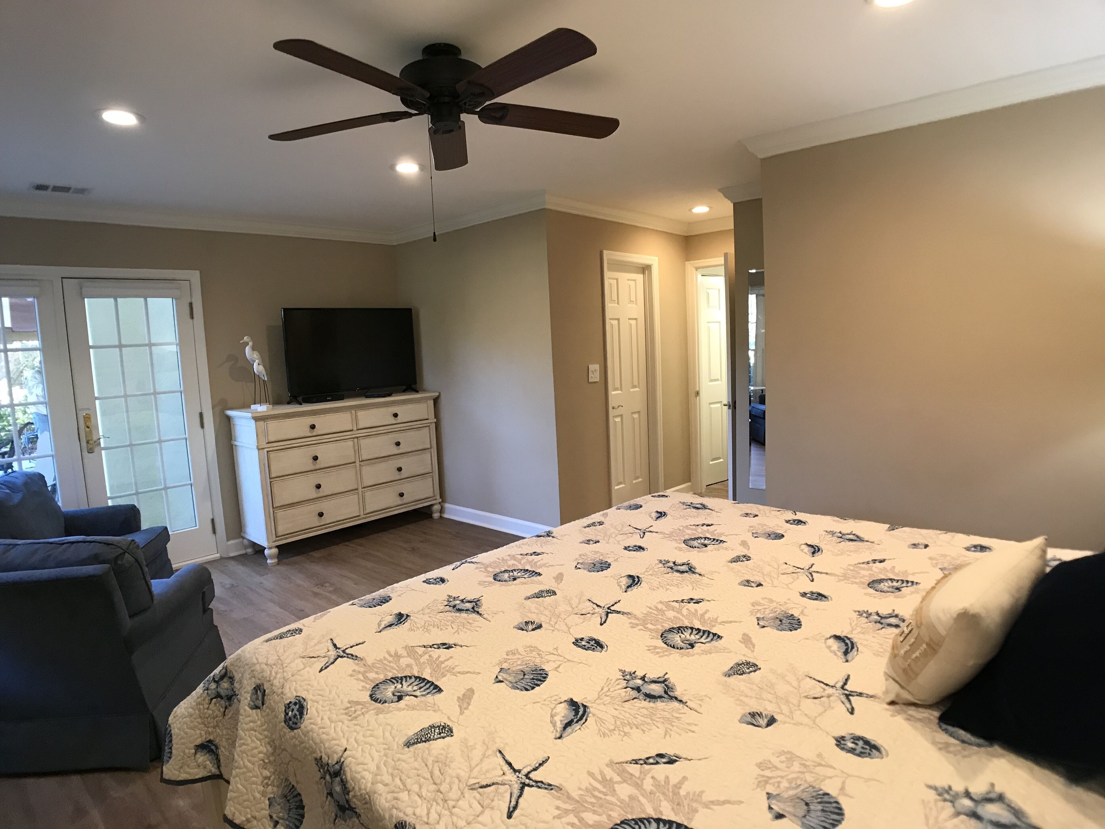 A bedroom with a bed, a dresser, a television, and a ceiling fan.