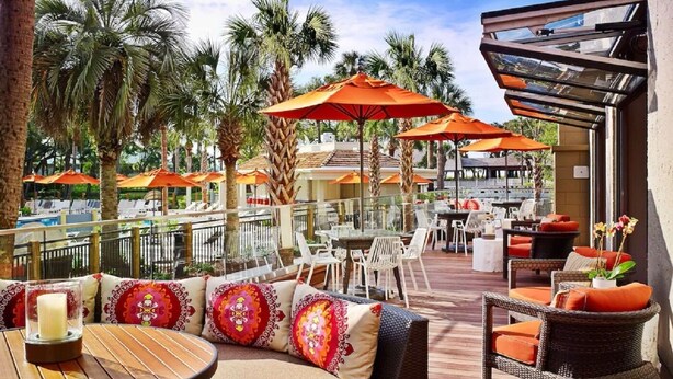 An outdoor patio with wooden flooring, wicker furniture, and orange umbrellas.