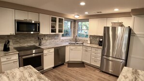 A modern kitchen with white cabinets, stainless steel appliances, and a marble countertop.