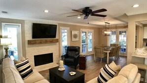 A living room with a fireplace, a television, and a dining area with a table and chairs.