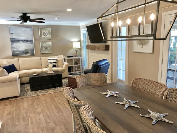 A spacious living room with a large wooden dining table, wicker chairs, a beige sofa, and a ceiling fan. - BEACH and GOLF RESORT Luxury Lagoon & Golf View Villa 2 Patios+KING BED (Hilton Head Island)