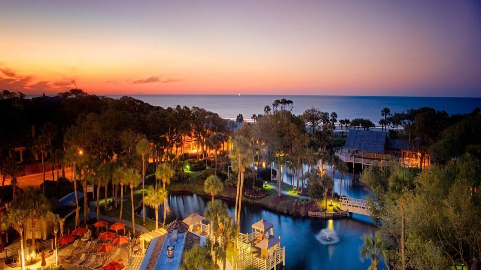 A resort with a pool, lounge chairs, and a sunset view.