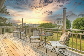 A wooden deck with outdoor furniture, a table with a plate of food, and a view of houses and trees in the background.