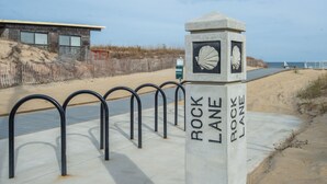 A concrete monument with the text "Rock Lane" and a shell design, located on a concrete path beside a sandy beach area. - Breathtaking Sunsets On Back Bay- Your Sandbridge Escape Awaits! (Virginia Beach)