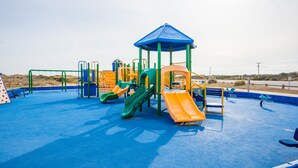 A playground with multiple slides and climbing structures, surrounded by a blue safety surface. - Breathtaking Sunsets On Back Bay- Your Sandbridge Escape Awaits! (Virginia Beach)