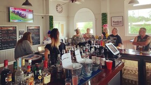Un bar avec un assortiment de bouteilles d’alcool, une caisse enregistreuse et un téléviseur diffusant un événement sportif.