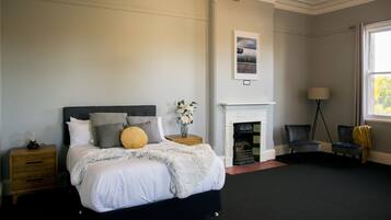 Een slaapkamer met een bed, nachtkastjes, een open haard, een stoel en een lamp.
