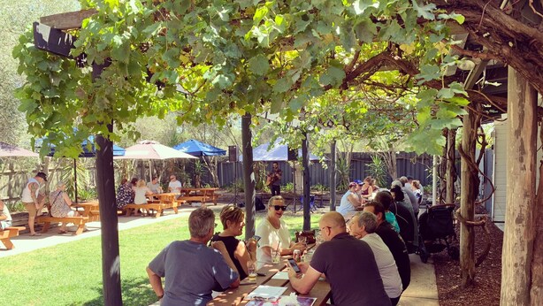 Un espace extérieur aménagé avec des tables et des bancs en bois, installé sous une pergola ombragée.